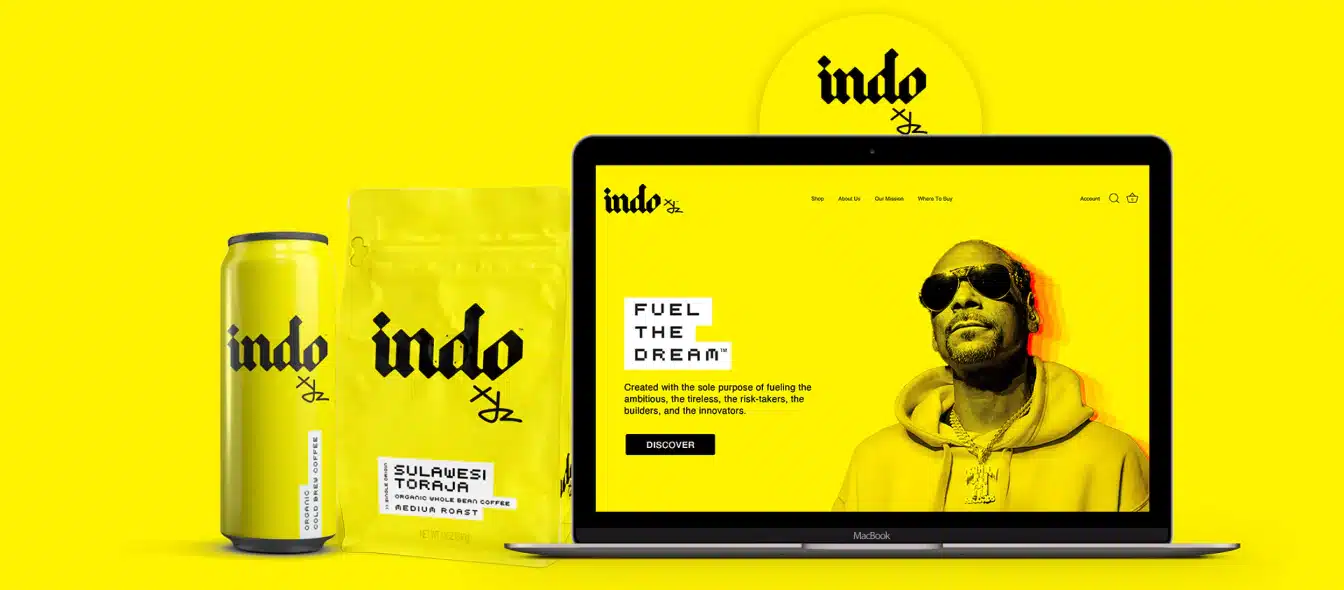 A bright yellow-themed display showcases Indo's brand products, including a coffee bag and can, next to a laptop showing Indo's website. The screen features a person in sunglasses with the words "FUEL THE DREAM" and a navigation menu visible on the top right.