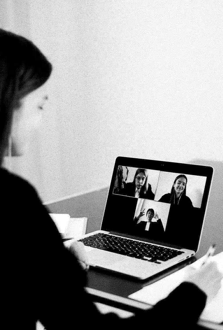 A person is participating in a video conference on a laptop, viewing three other individuals, each in their own video tiles. Our approach emphasizes engaging discussions, with one person actively gesturing while speaking. The setting appears to be a home or office.