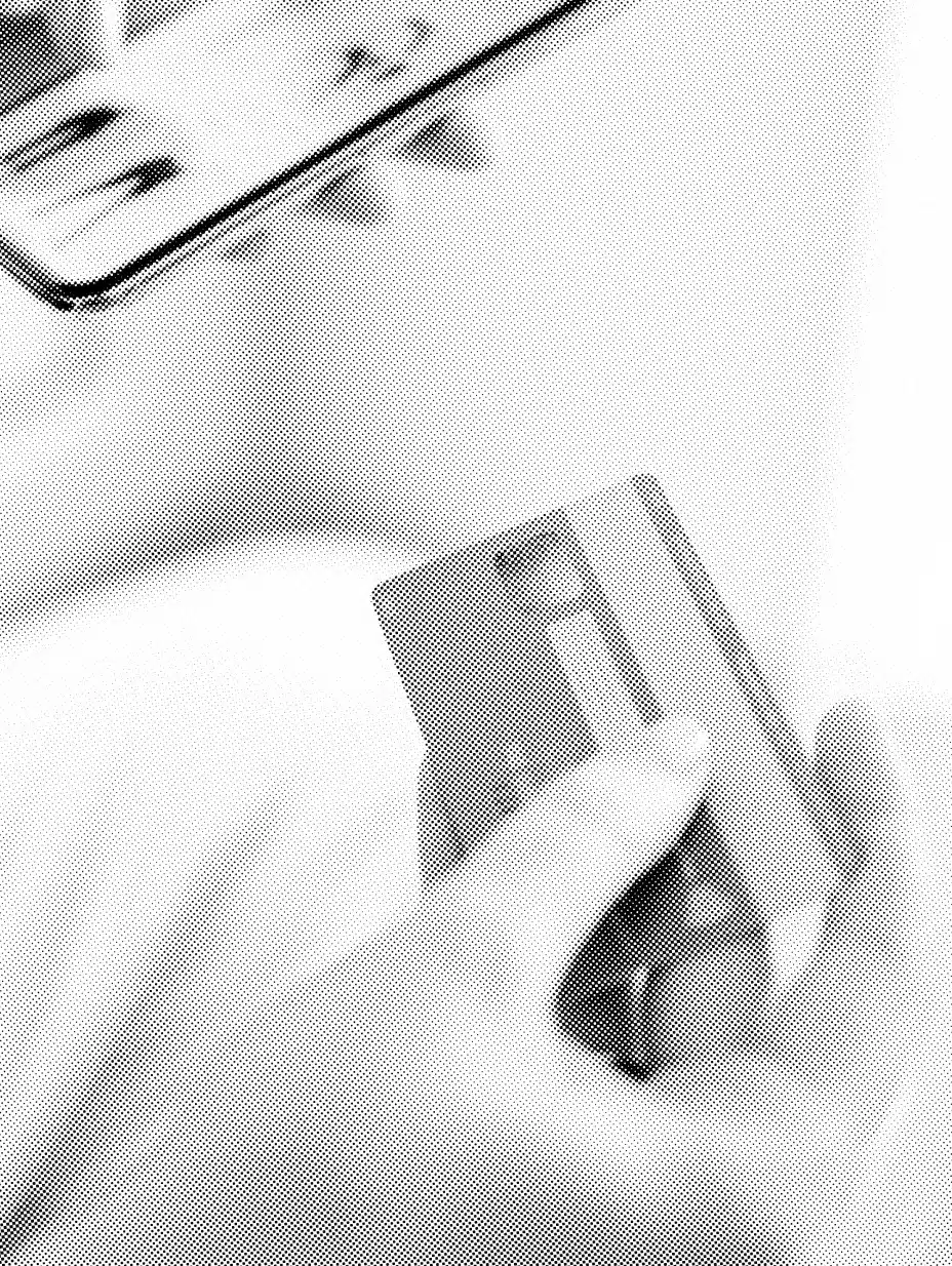 A person holds a credit card in their hand, preparing to make a purchase. The top section of the card is visible, showing part of the magnetic strip and chip. In the background, there is a blurred view of a smartphone or a tablet screen—a modern scene reflecting contemporary commerce practices.
